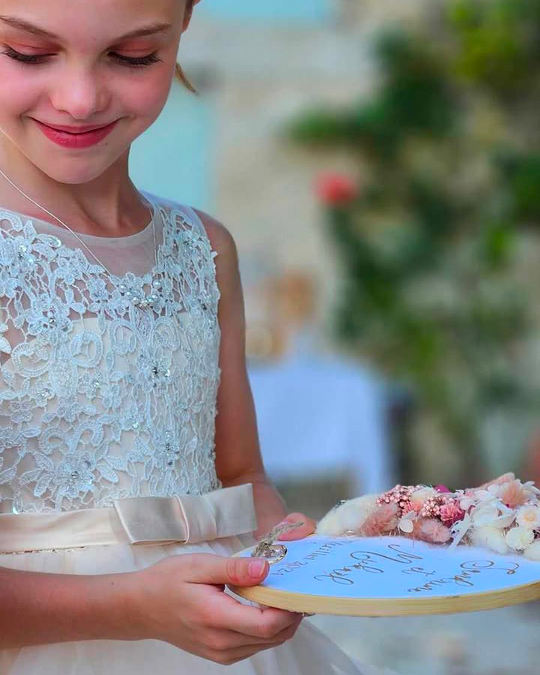 petite fille souriante en tenue de mariage tenant dans la main un porte alliance en fleurs séchées